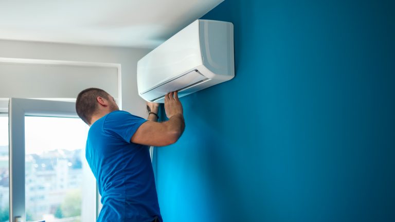 Eine Person kontrolliert eine offenbar frisch angebrachte Split-Klimaanlage, die an einer Wand h&auml;ngt.