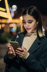 Eine Person steht nachts auf der Straße und blickt auf ihr Smartphone.