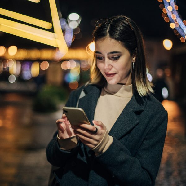 Eine Person steht nachts auf der Stra&szlig;e und blickt auf ihr Smartphone.