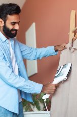 Eine Person nutzt einen Steamer an einem Hemd.