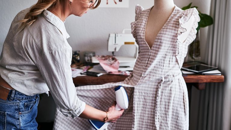 Eine Person nutzt eine Dampfb&uuml;rste an einem Kleid auf einer Kleiderpuppe.