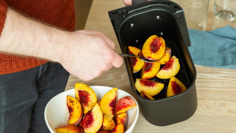 Eine Person nimmt mit einem L&ouml;ffel Fr&uuml;chte aus dem Korb eines Airfryers.