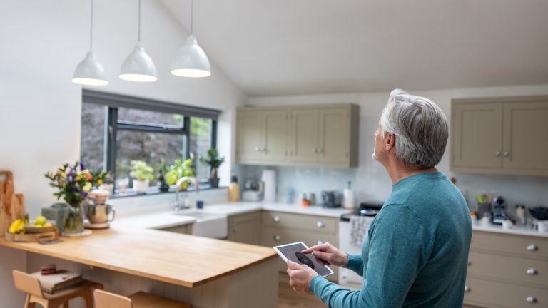 Eine Person steht in der K&uuml;che und bedient ein Tablet, um die Beleuchtung anzupassen.