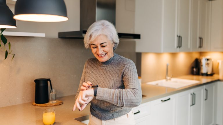 Eine Person steht in der K&uuml;che und schaut l&auml;chelnd auf ihre Smartwatch.