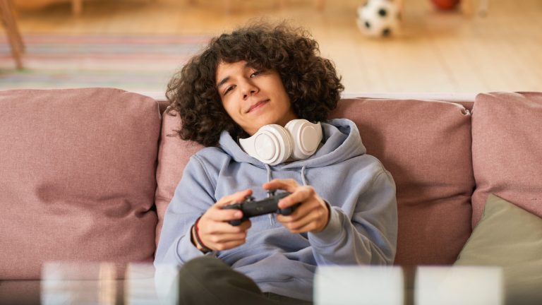 Eine Person sitzt auf einem Sofa und h&auml;lt einen Controller in der Hand.