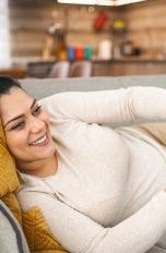 Eine Person liegt gemütlich auf einem Sofa und hält einen Controller in der Hand.