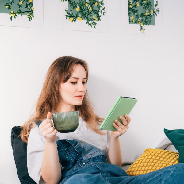 Eine Person h&auml;lt eine Tasse in der Hand, w&auml;hrend sie auf einem E Book-Reader liest.