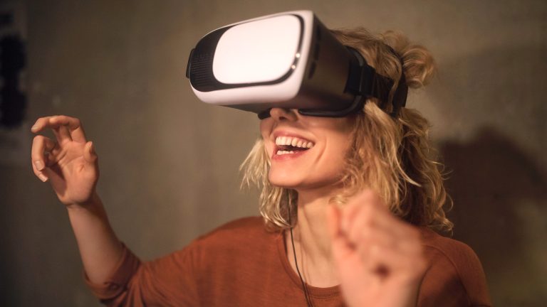 Eine Person tr&auml;gt eine VR-Brille und lacht dabei vergn&uuml;gt.