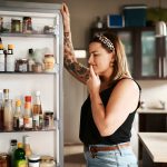 Eine Person steht gr&uuml;belnd vor einem ge&ouml;ffneten K&uuml;hlschrank.