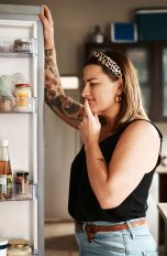 Foodwaste, So vermeidest du es, Lebensmittel wegzuschmeißen Eine Person steht grübelnd vor einem geöffneten Kühlschrank.