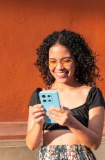 Handyhülle, So findest du die richtige Eine Person steht im Freien vor einer einfarbigen Wand und hält ein Smartphone in einer Hülle in der Hand.