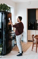 Kühlschränke ab 700 Euro, die besten Premium-Modelle Ein Mensch steht in der Küche vor seinem Kühlschrank und tippt etwas auf einem Display darauf ein.