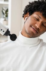 Massagegeräte, Die verschiedenen Typen und Tipps zur Entspannung Eine Person gönnt sich eine Nackenmassage mit einer Massagepistole.