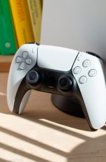 PS5 als Primär aktivieren, So machst du es Bild einer PS5 mitsamt Dualsense-Controller, die im Sonnenlicht auf einem Holzboden steht.