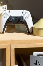 PS5 vs. PS5 Slim vs. PS5 Pro, So unterscheiden sich die Versionen Ein Dualsense-Controller steht in einem Regal. Im Vordergrund ist eine PS5 zu erkennen.