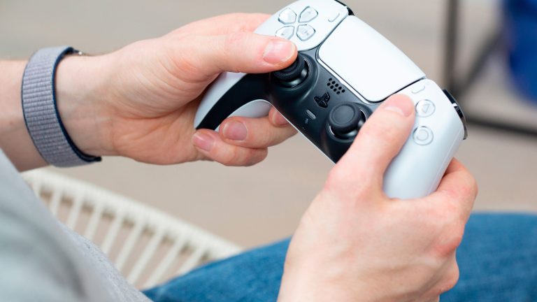 PS5 als Primär aktivieren, So machst du es Eine Person hält einen Dualsense-Controller in der Hand.