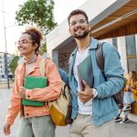 Zwei Personen entfernen sich von der Uni und tragen Arbeitsmaterial in den H&auml;nden.