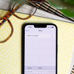 Ein iPhone liegt neben einer Brille auf einem Tisch. Auf dem Display ist das &Auml;ndern des Ger&auml;tenamens zu sehen.