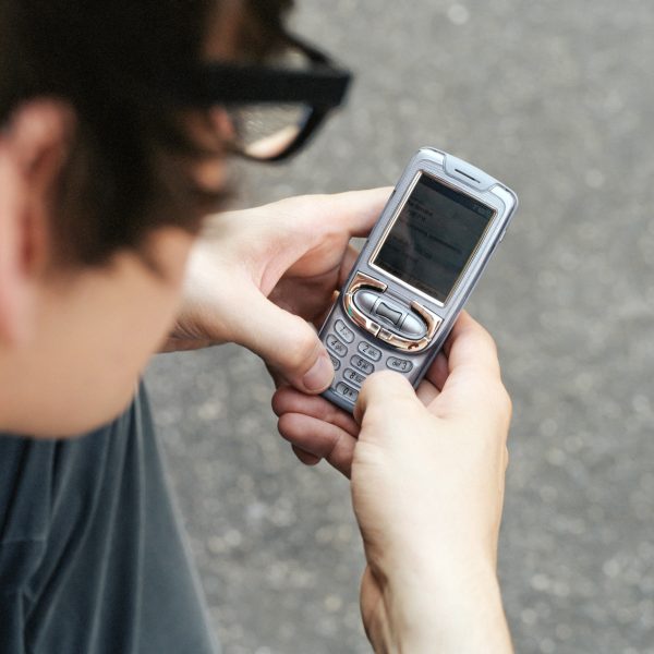 Eine Person h&auml;lt ein altes Mobiltelefon mit Tasten in der Hand und schreibt darauf eine Nachricht.