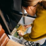 Eine Person legt eine durchsichtige T&uuml;te mit buntem Gem&uuml;se in die Schublade eines Gefrierschrankes.