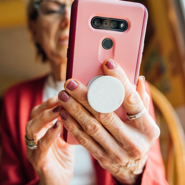Eine Person h&auml;lt ein Smartphone mithilfe eines PopSockets in der Hand. Der Fokus der Aufnahme liegt auf der R&uuml;ckseite des Smartphones sowie den H&auml;nden der Person.