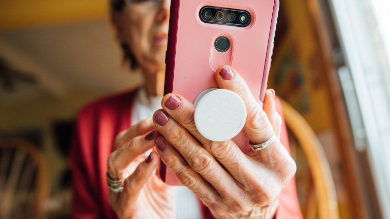 Eine Person h&auml;lt ein Smartphone mithilfe eines PopSockets in der Hand. Der Fokus der Aufnahme liegt auf der R&uuml;ckseite des Smartphones sowie den H&auml;nden der Person.