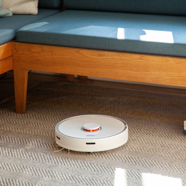 Ein Roborock S5 Max f&auml;hrt &uuml;ber einen Teppich vor einer Sitzbank.