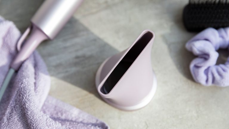 Nahaufnahme des Stylingd&uuml;senaufsatzes. Er liegt auf einem Badezimmerschrank; im Hintergrund ist der F&ouml;hn, ein Handtuch sowie ein Haargummi zu erkennen.