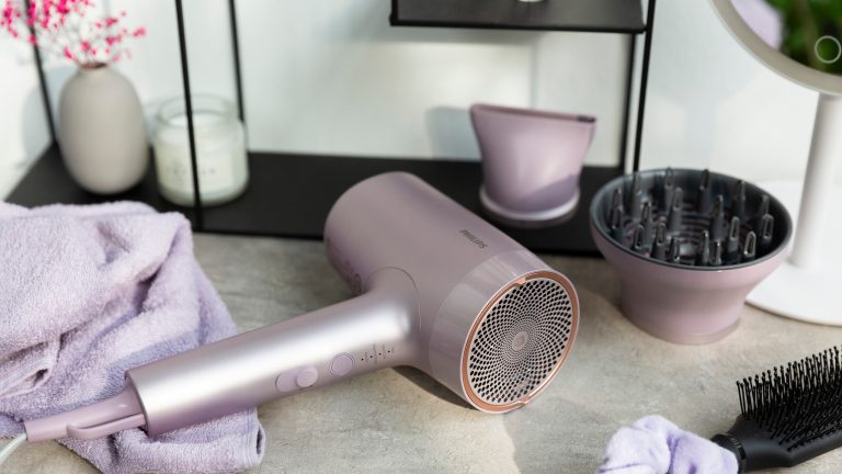 Der Haartrockner Philips 7000er liegt auf einem Tisch im Badezimmer umgeben von verschiedenem Zubeh&ouml;r, wie seinen Aufs&auml;tzen, einer B&uuml;rste und einem Haargummi.