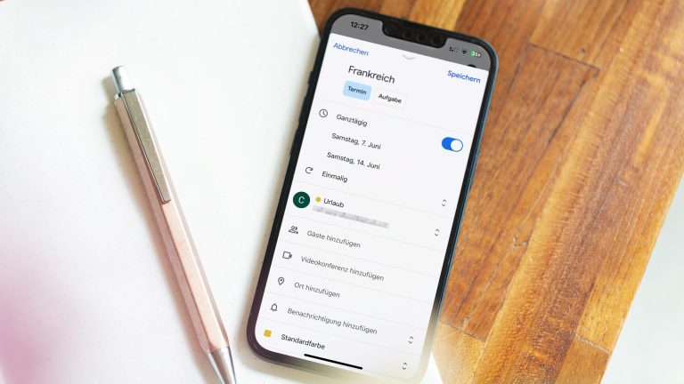 Ein iPhone liegt auf einem Notizblock. Auf dem Display ist ein erstellter Eintrag im Google Kalender f&uuml;r einen Urlaub zu sehen.