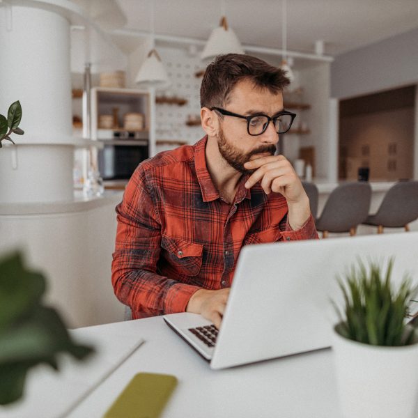 Eine Person sitzt in einer offenen Küche an einem Tisch und bedient einen Laptop.