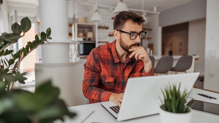 Eine Person sitzt in einer offenen Küche an einem Tisch und bedient einen Laptop.