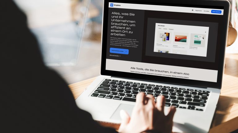 R&uuml;ckansicht einer Person, die vor einem ge&ouml;ffneten Notebook sitzt. Der Screen zeigt die Dropbox-Startseite.