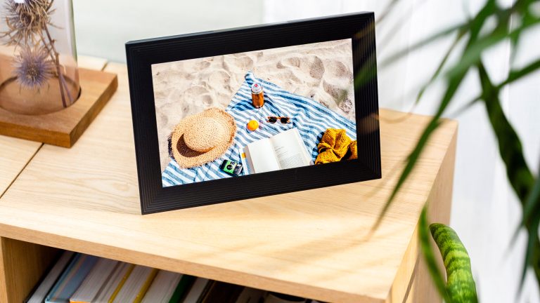 Ein digitaler Bilderrahmen steht auf einem B&uuml;cherregal. Er zeigt das Foto einer Strandszene.