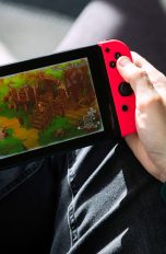 Nintendo Switch Online, Tarife, Vorteile und mehr Eine Person hält eine Nintendo Switch in der Hand und spielt darauf ein Cozy Game.