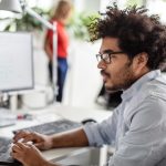 Eine Person sitzt in einem B&uuml;ro vor einem Laptop und nutzt das Touchpad.