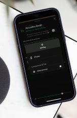 AirPlay, So funktioniert das drahtlose Streaming von Apple Ein iPhone liegt neben einem Lautsprecher auf einer Tischkante. Darauf sind die AirPlay-Einstellungen mit einer Verbindung zu einem Lautsprecher in einem Wohnzimmer zu sehen.