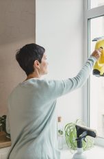 Fenstersauger, 6 Geräte für streifenfreie Sauberkeit Eine Person steht in einer Küche vor dem Fenster und zieht mit einem Fenstersauger die Fensterscheibe von innen ab.