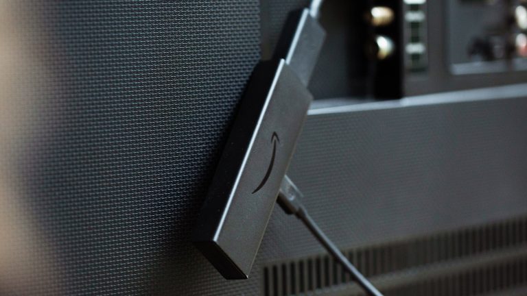 Handy mit Fernseher verbinden, So klappt es bei iOS und Android Ein Amazon Fire TV Stick hängt mit einem Kabel angeschlossen auf der Rückseite eines Fernsehers.