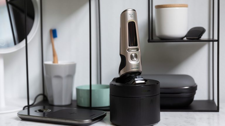 Ein Philips S9000 Prestige Rasierer steht in einem Quick Clean Pod auf einer Anrichte in einem Badezimmer. Daneben liegt das zugeh&ouml;rige Ladepad.
