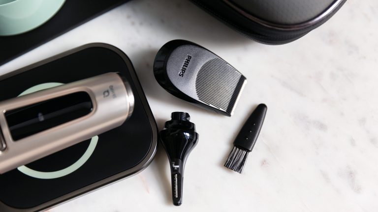 Ein Philips S9000 Prestige liegt auf dem QI-Ladepad. Daneben liegen ein Nasen- und Ohrhaartrimmer-Aufsatz, ein Bartstyler-Aufsatz und ein kleiner Pinsel.