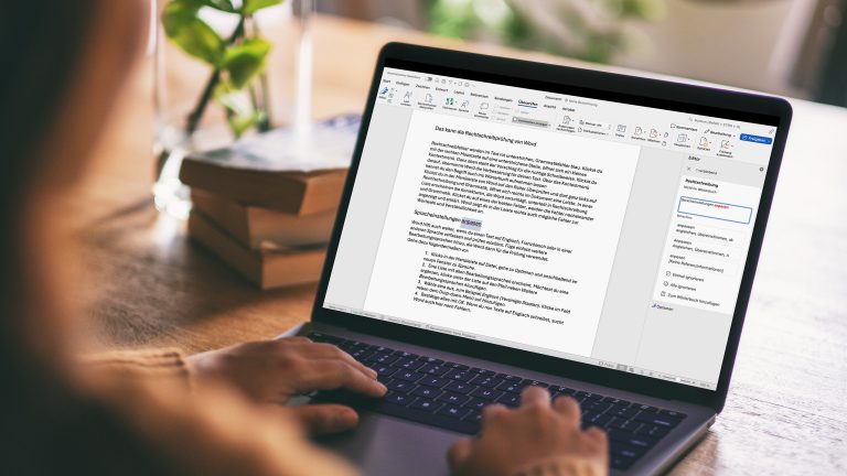 Die Hände einer Person liegen auf der Tastatur eines Notebooks auf dessen Display ein geöffnetes Word-Dokument zu sehen ist.