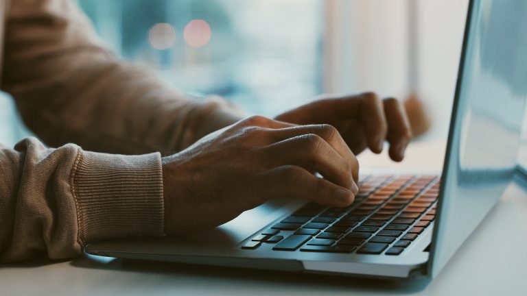 Seitenansicht eines Notebooks auf dessen Tastatur die Hände einer Person liegen.