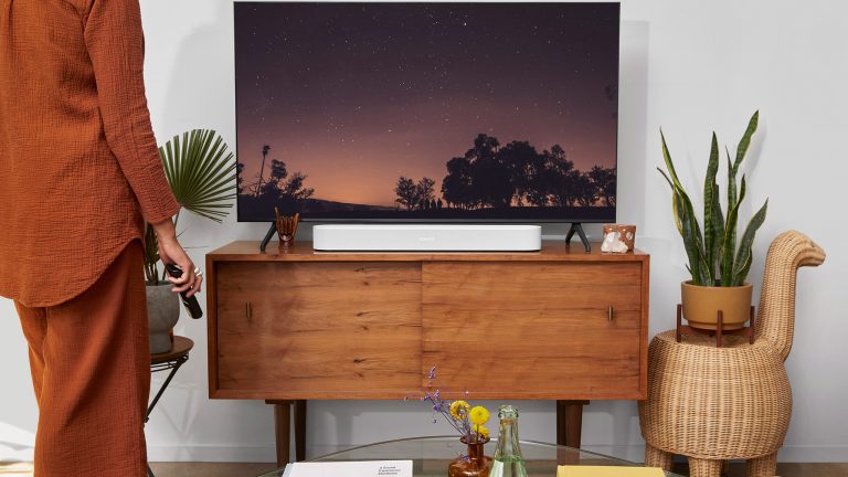 Sonos zurücksetzen, So funktioniert es bei Move, One & Co. Eine Person steht vor einem Fernseher, unter dem ein Sonos Beam steht.