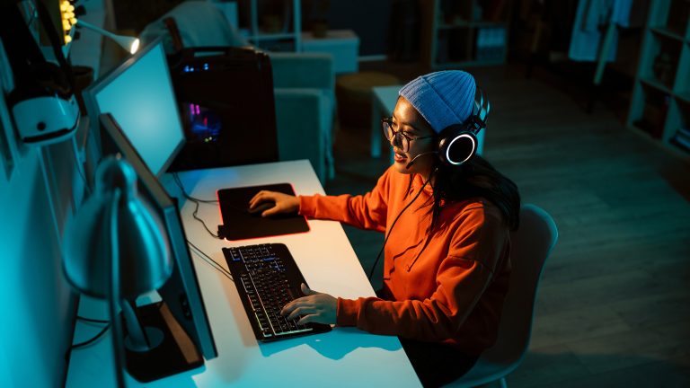 Eine Person sitzt an einem Schreibtisch vor einem Gaming-Setup und kommuniziert per Headset.