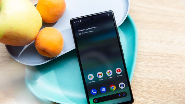 Das Google Pixel 6a liegt auf zwei pastellfarbenen Sch&uuml;sseln. Im Hintergrund ist etwas Obst zu sehen.