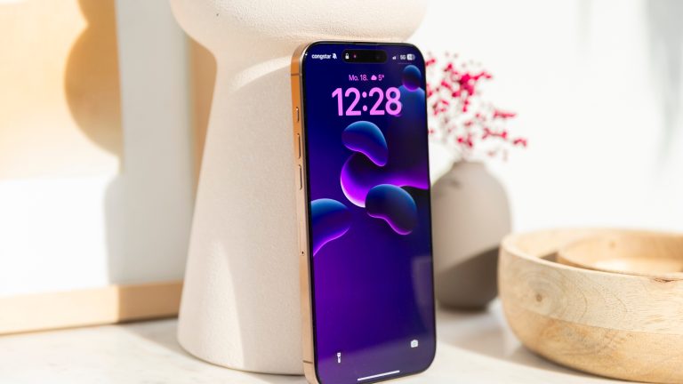 Ein iPhone 16 Pro Max in Wüstensand steht an eine Vase gelehnt auf einem Regal.