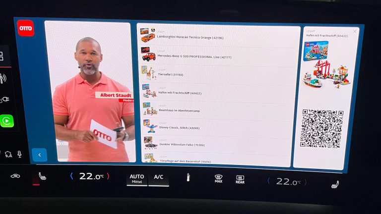 Eine Nahaufnahme eines integrierten Displays in einem Auto. Darauf ist ein Live Shopping Stream von OTTO zu sehen: links ein Moderator, mittig eine Auflistung von Produkten und rechts ein einzelnes Produkt mit einem QR Code.