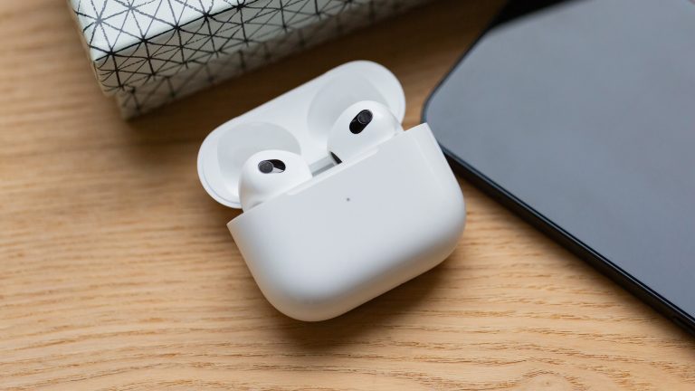 Ein offenes Ladecase mit zwei AirPods darin, daneben liegt ein iPhone auf einem Holzuntergrund.