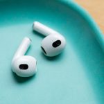 Zwei AirPods liegen in einer t&uuml;rkisfarbenen Schale auf einem Holzuntergrund.